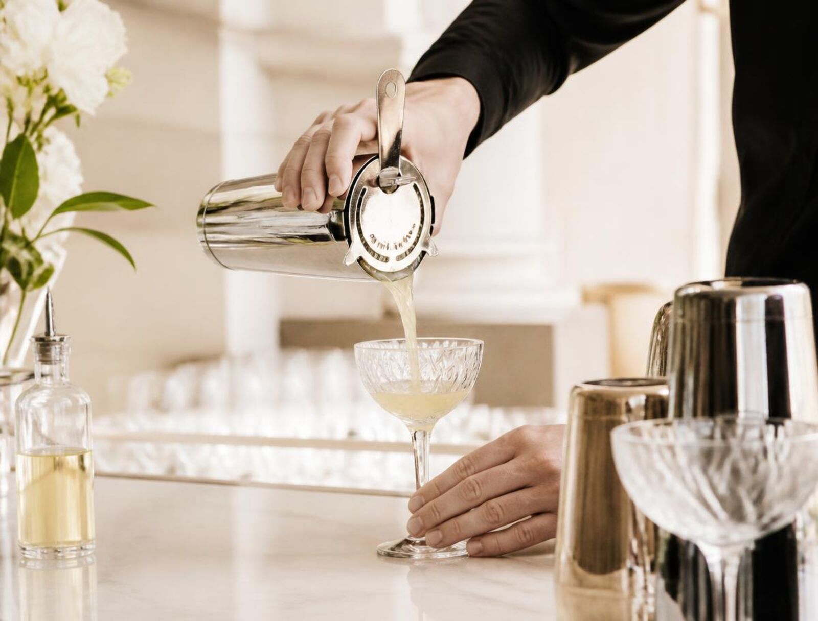 Illustrative photo of a bartender in black attire pouring a cocktail